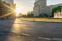 the sun is shining over a street and water feature fountain in the background of a big building