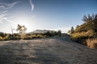 the sun is shining on a road with gravel and bushes in the foreground and mountains