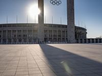 the sun shining through a large building with an olympic symbol on it's side