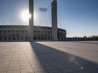 the sun shining through a large building with an olympic symbol on it's side