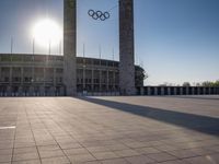 the sun shining through a large building with an olympic symbol on it's side