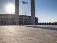 the sun shining through a large building with an olympic symbol on it's side