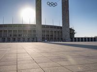 the sun shining through a large building with an olympic symbol on it's side