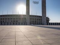 the sun shining through a large building with an olympic symbol on it's side