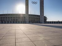 the sun shining through a large building with an olympic symbol on it's side