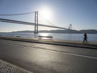 the sun shining over the water and a bridge across from it with benches on a curb beside it