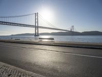 the sun shining over the water and a bridge across from it with benches on a curb beside it