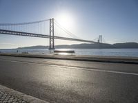 the sun shining over the water and a bridge across from it with benches on a curb beside it