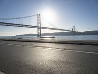 the sun shining over the water and a bridge across from it with benches on a curb beside it