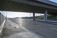 street under a highway with the sun shining down on it and cars parked in front of it