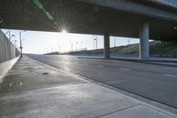 street under a highway with the sun shining down on it and cars parked in front of it