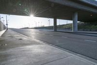 street under a highway with the sun shining down on it and cars parked in front of it