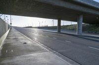 street under a highway with the sun shining down on it and cars parked in front of it