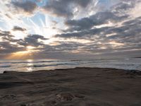 there is a surfer that is walking across the rocks under a stormy sky at sunset