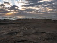 there is a surfer that is walking across the rocks under a stormy sky at sunset