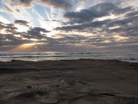 there is a surfer that is walking across the rocks under a stormy sky at sunset