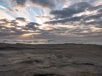 there is a surfer that is walking across the rocks under a stormy sky at sunset