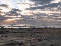 there is a surfer that is walking across the rocks under a stormy sky at sunset