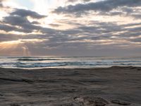 there is a surfer that is walking across the rocks under a stormy sky at sunset