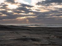 there is a surfer that is walking across the rocks under a stormy sky at sunset