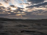 there is a surfer that is walking across the rocks under a stormy sky at sunset