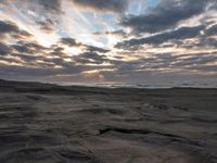 there is a surfer that is walking across the rocks under a stormy sky at sunset