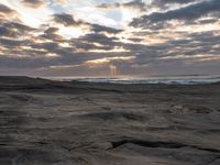 there is a surfer that is walking across the rocks under a stormy sky at sunset