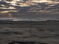 there is a surfer that is walking across the rocks under a stormy sky at sunset