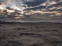 there is a surfer that is walking across the rocks under a stormy sky at sunset