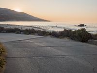 a person riding a surf board down the side of a road near the ocean at sunset