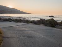 a person riding a surf board down the side of a road near the ocean at sunset