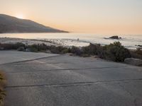 a person riding a surf board down the side of a road near the ocean at sunset