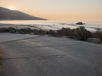 a person riding a surf board down the side of a road near the ocean at sunset