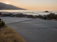 a person riding a surf board down the side of a road near the ocean at sunset