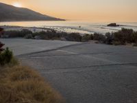 a person riding a surf board down the side of a road near the ocean at sunset