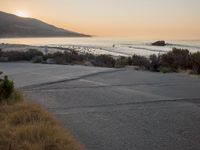 a person riding a surf board down the side of a road near the ocean at sunset