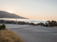 a person riding a surf board down the side of a road near the ocean at sunset