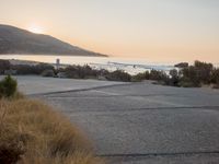 a person riding a surf board down the side of a road near the ocean at sunset