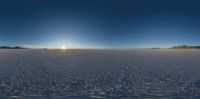 an alien like landscape with the sun rising behind it and footprints in the snow with some grass, rocks and mountains