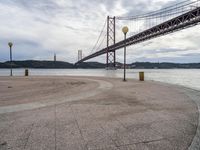 the suspension bridge is near the water in front of a building and mountain ranges and blue sky