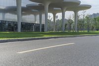 a person rides a motorcycle past a building, in the middle of a road with many tall structures on it