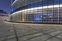 a view of a large office building at night from outside the building with cobblestone pavement in front of it