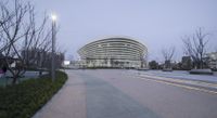 a building with a curved ramp to the right is lit up at twilight in a downtown area