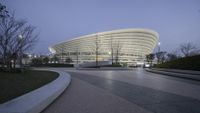 a building with a curved ramp to the right is lit up at twilight in a downtown area