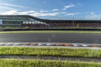 an empty track next to tall green grass and a building in the background with blue skies