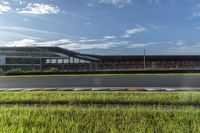 an empty track next to tall green grass and a building in the background with blue skies