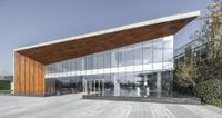 an exterior of a building with large glass walls and a long wooden roof that covers the front