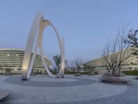 two large circular steel sculptures near a circular courtyard in front of building in the background