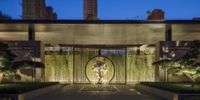 a sculpture stands in an outdoor area next to a building with a courtyard and trees