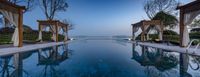 a pool sits with chairs overlooking the ocean and lights in front of it at dusk